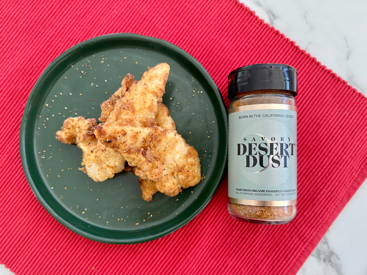 Golden fried chicken tenders on a green plate beside a Savory Desert Dust jar on a red cloth.
