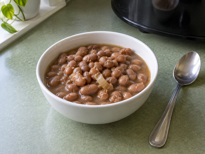 Tender pinto beans with onion and light broth in a white bowl on a sage-green kitchen counter.