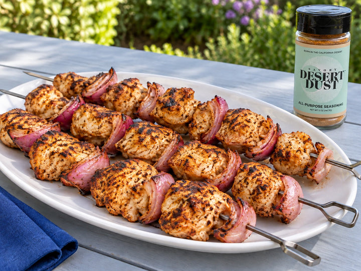 Grilled chicken and red onion kabobs on a white platter beside a Savory Desert Dust jar.