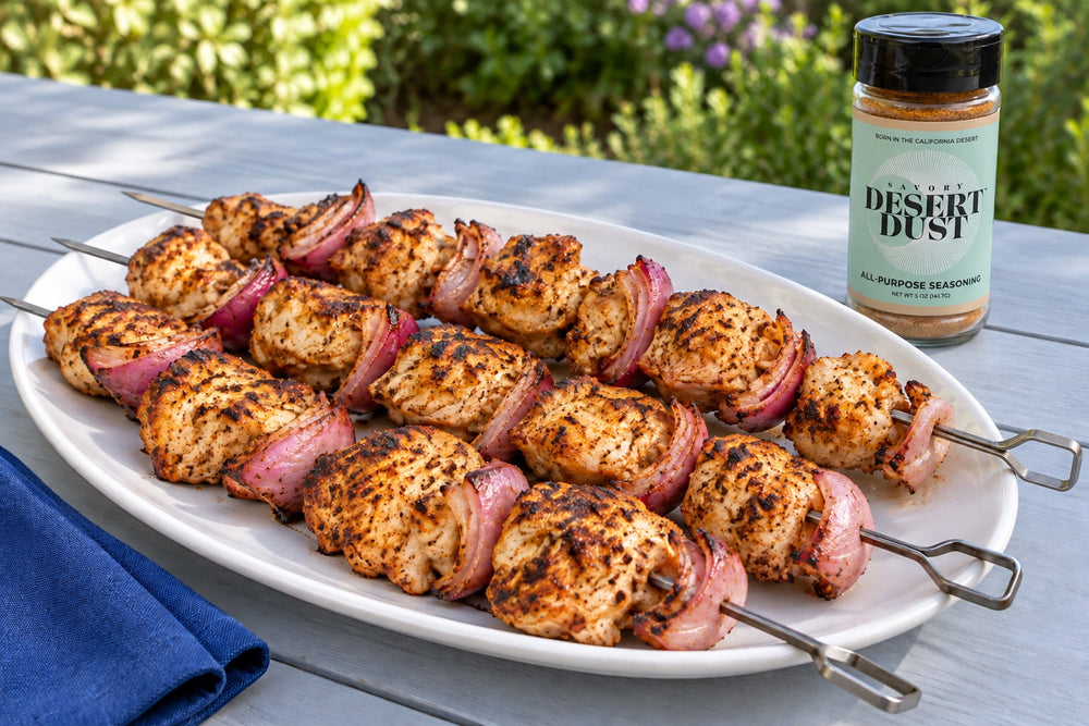 Grilled chicken and red onion kabobs on a white platter beside a Savory Desert Dust jar.