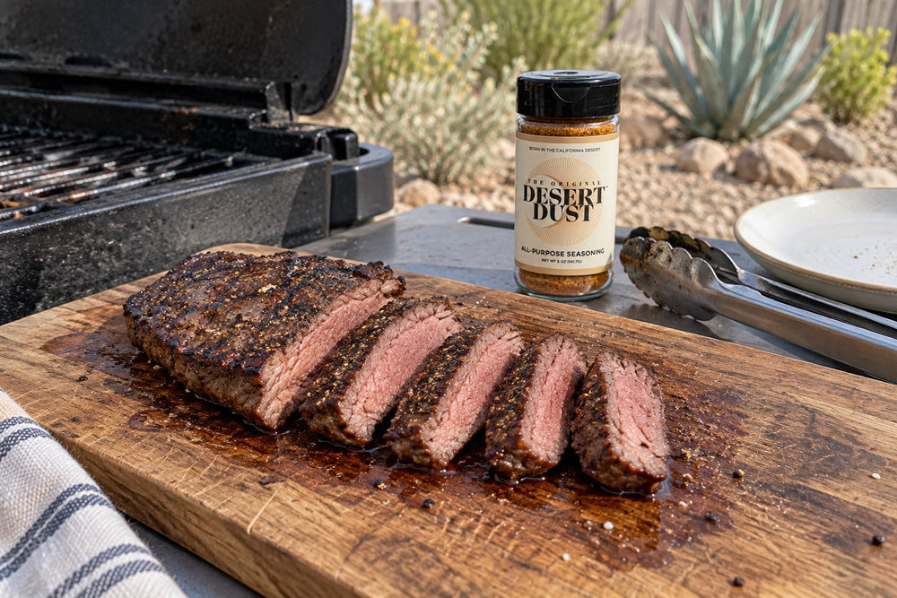 Sliced grilled flat iron steak on a board beside a backyard grill