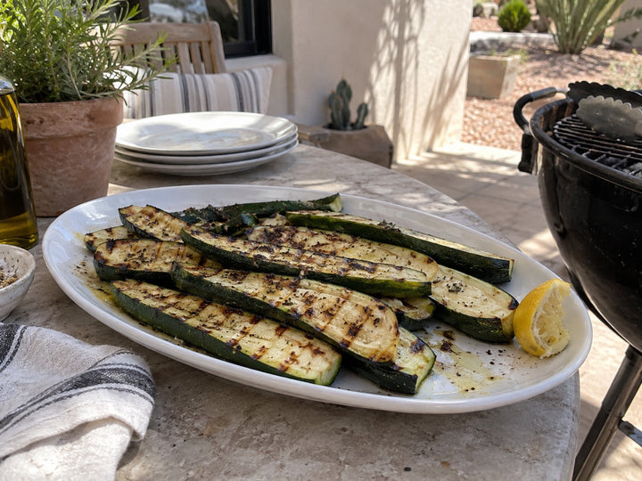 Grilled zucchini with lemon on a white platter beside a grill