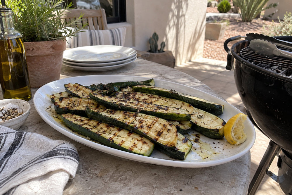 Grilled zucchini with lemon on a white platter beside a grill