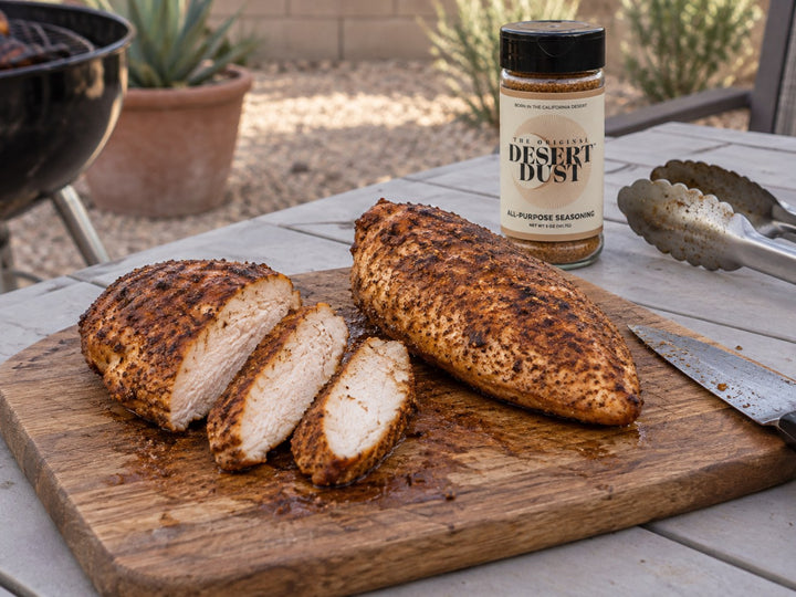 Smoked chicken breasts partly sliced on a backyard table beside Original Desert Dust