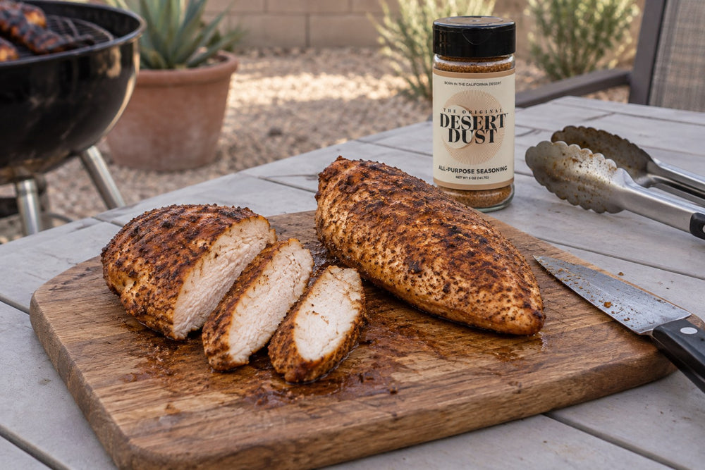 Smoked chicken breasts partly sliced on a backyard table beside Original Desert Dust