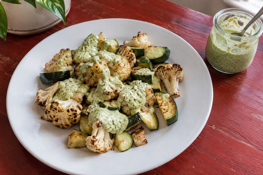 Poblano cream sauce spooned over roasted cauliflower and zucchini on a white plate