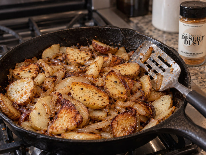 Fried potatoes and onions in a cast iron skillet beside Original Desert Dust
