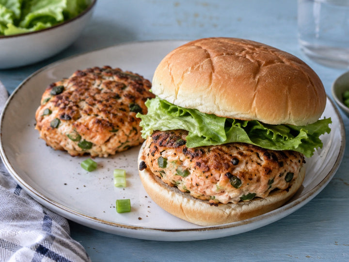 Homemade salmon burger with lettuce in a soft bun, with another cooked salmon patty alongside.