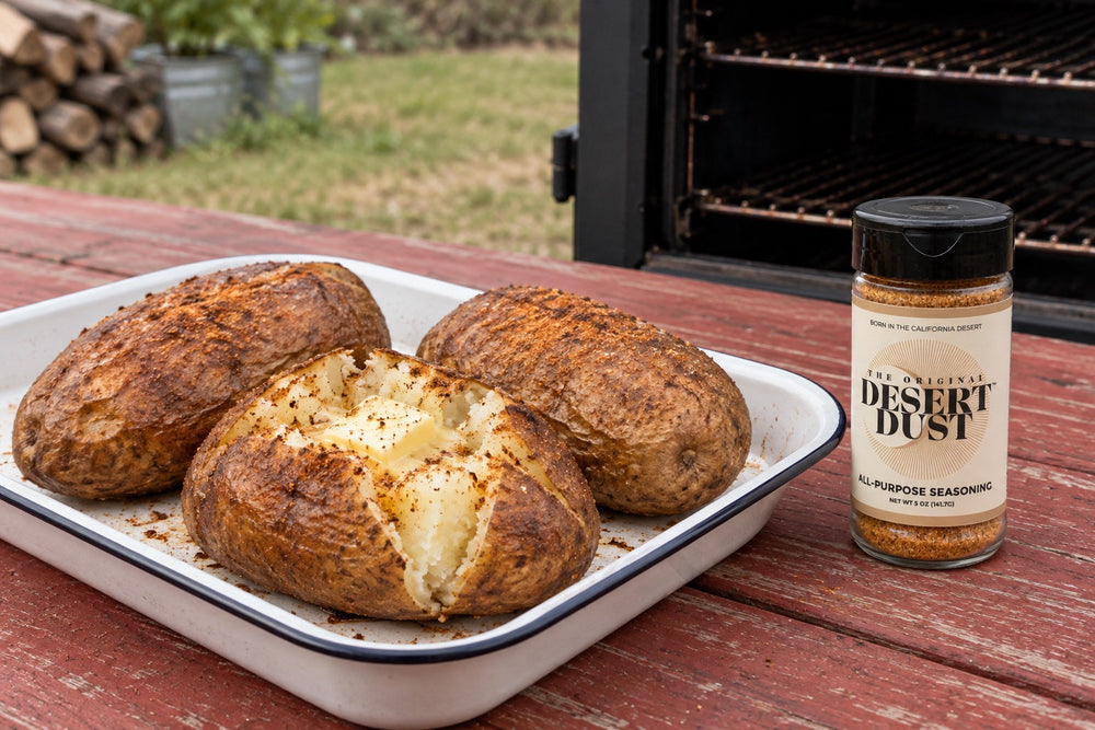 Split smoked russet potatoes with fluffy centers beside an Original Desert Dust jar and a backyard smoker.