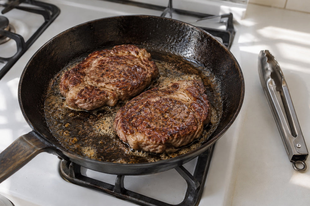 Two modest pan-cooked chuck-eye steaks with browned crusts in a skillet on a home kitchen stovetop.