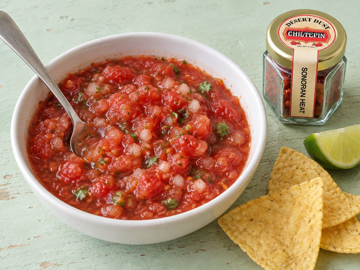 Fresh tomato Chiltepin salsa in a white bowl beside corn chips and the small Desert Dust Chiltepin jar.