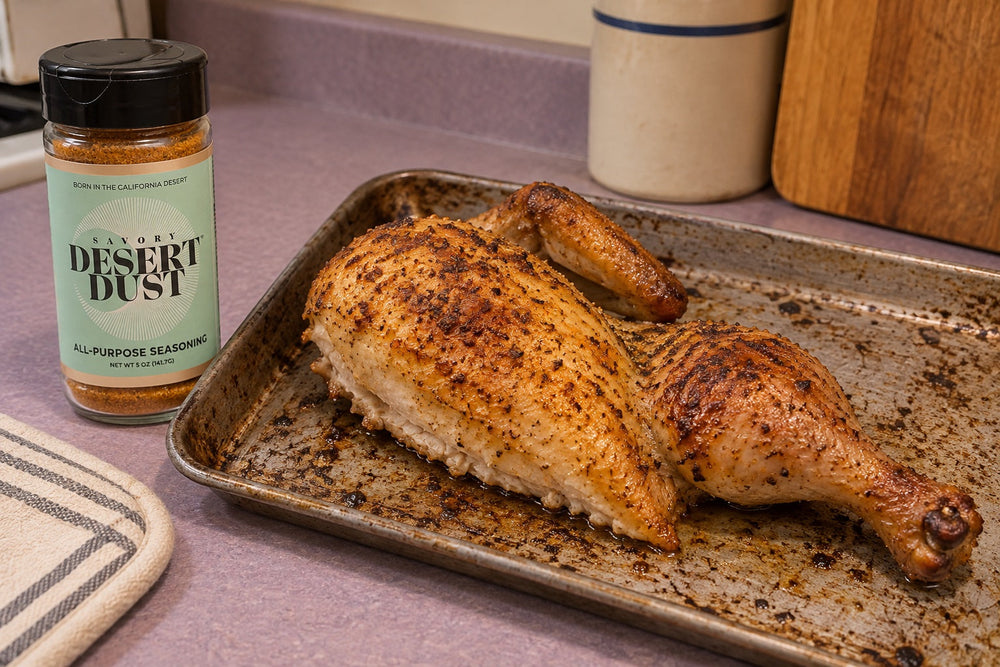 One roasted chicken half with a single breast, wing and leg on a small tray beside a Savory Desert Dust jar.