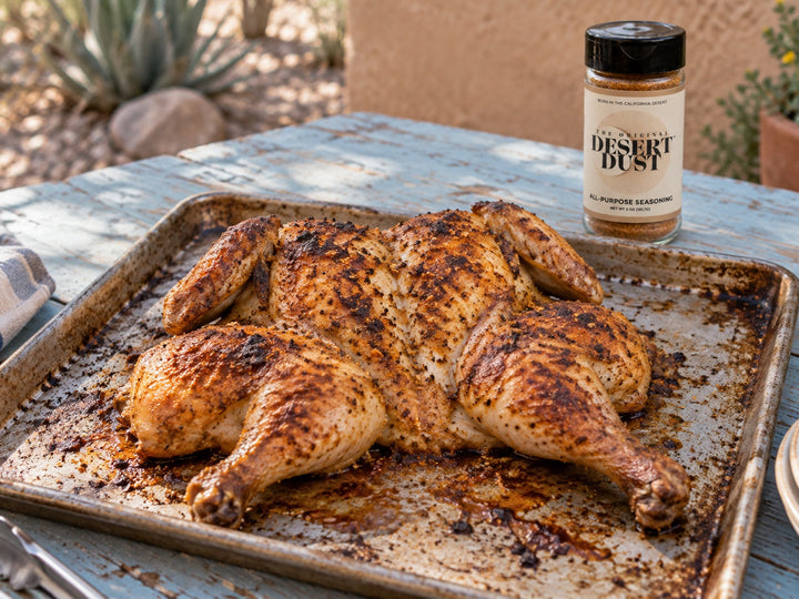 Roasted flattened spatchcock chicken on a baking tray on a desert patio. Original Desert Dust jar nearby.