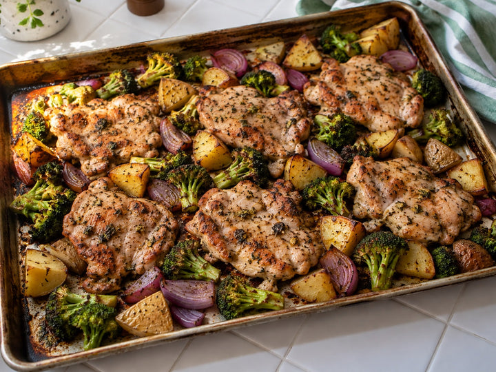 Roasted boneless skinless chicken thighs with potatoes, broccoli and red onion on a sheet pan.