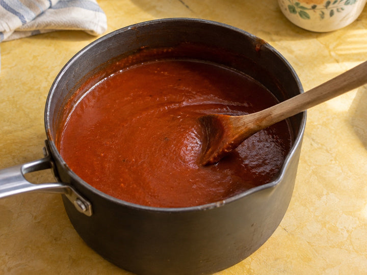 Smooth red enchilada sauce in a small saucepan on a yellow kitchen surface.