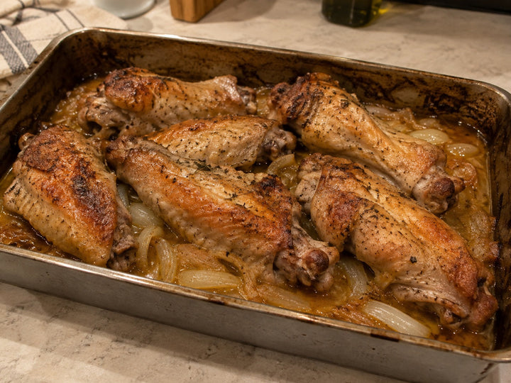 Baked turkey wing sections with browned skin, soft onions and cooking juices in a roasting pan.