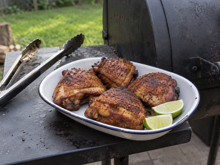 Smoked chicken thighs with lime beside a backyard smoker