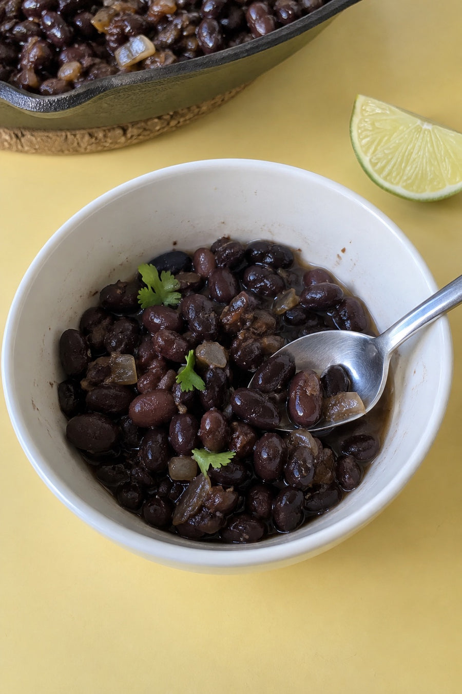 A spoonful of black beans with onion and cilantro in a white bowl beside a lime wedge.