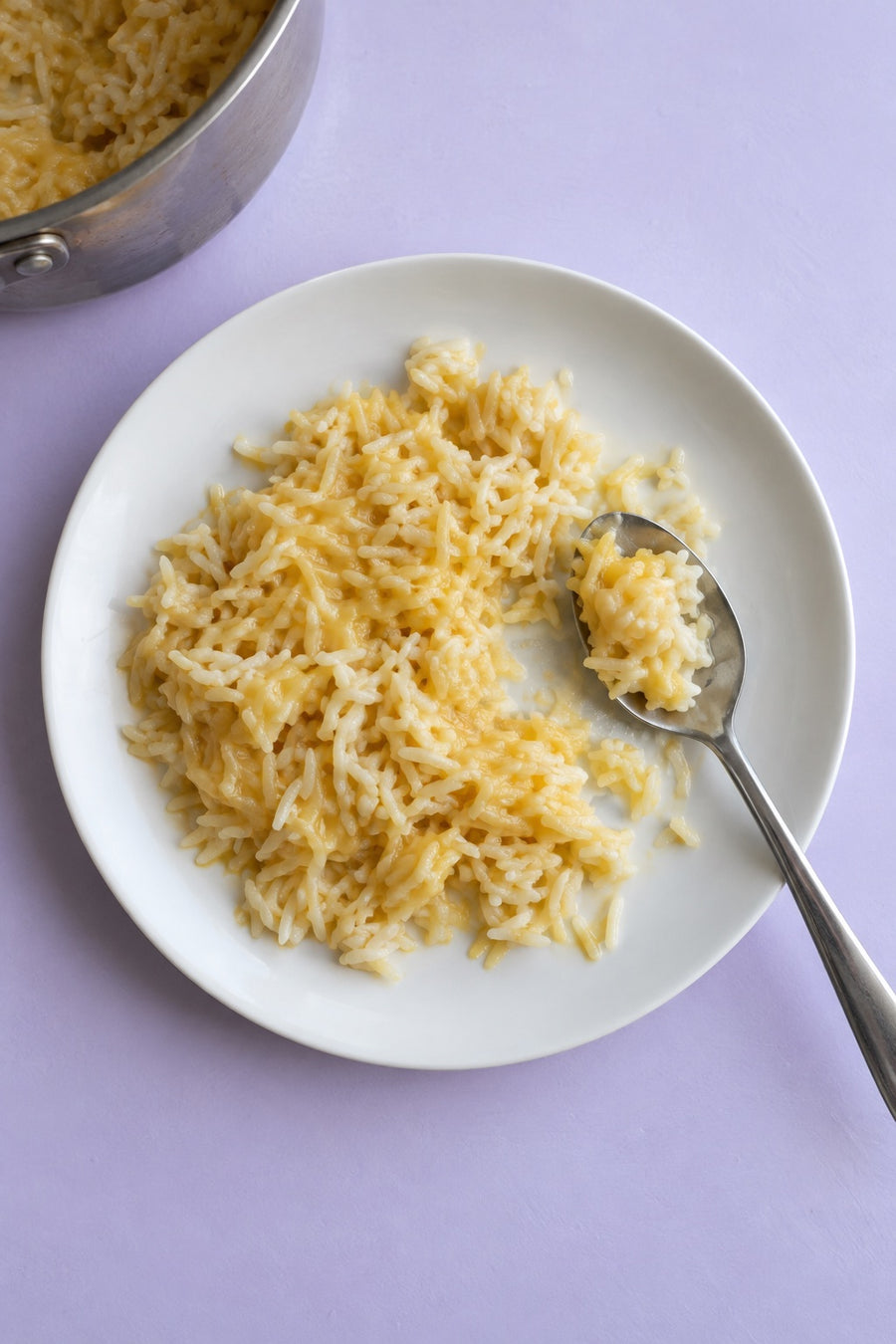 Overhead view of creamy cheddar rice on a white plate with a small spoonful at the edge.