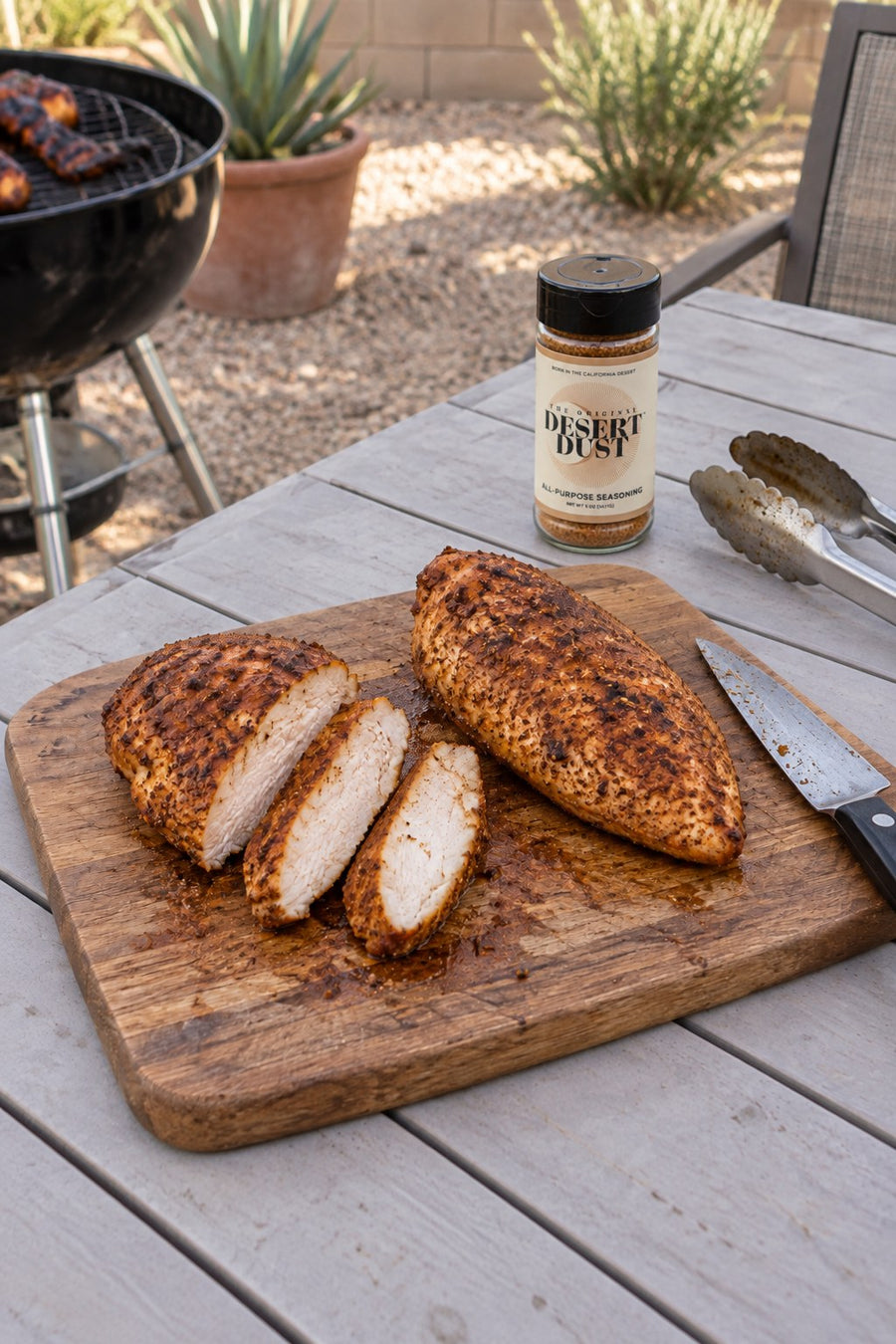 Smoked chicken breasts partly sliced on a backyard table beside Original Desert Dust