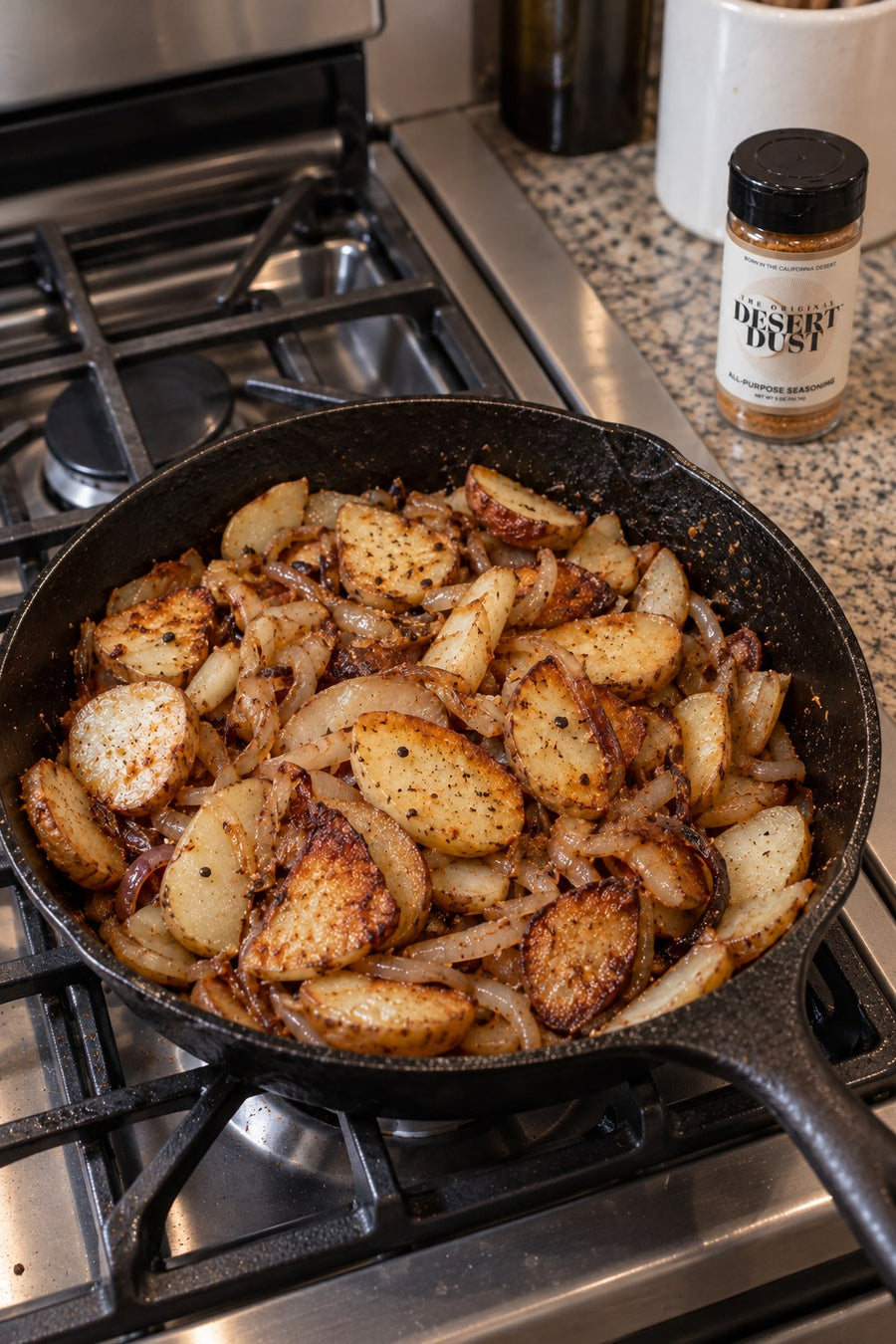 Fried potatoes and onions in a cast iron skillet beside Original Desert Dust