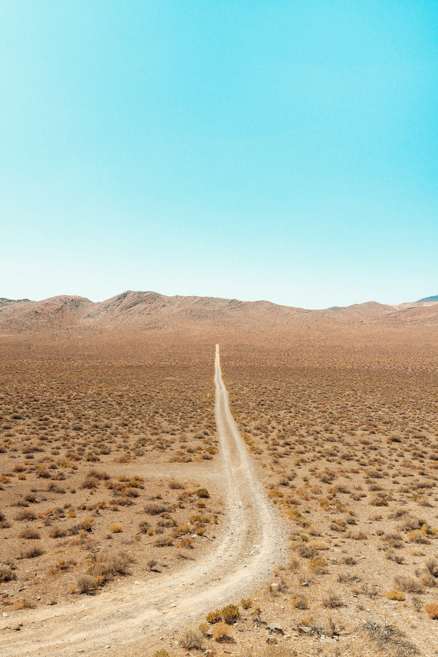 A narrow dirt road crossing an open desert valley