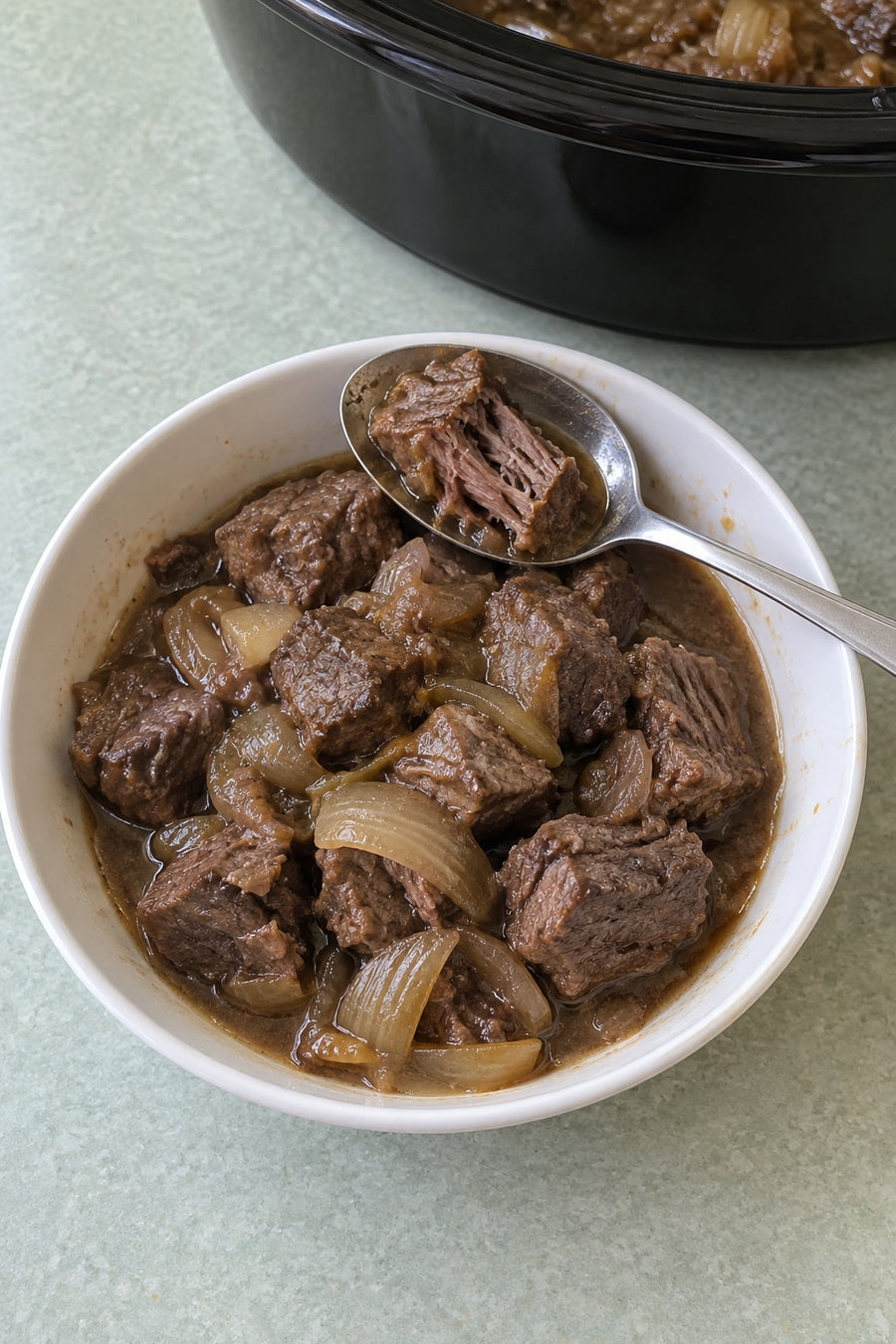 A spoonful of braised chuck beef with onion gravy over a small white bowl.
