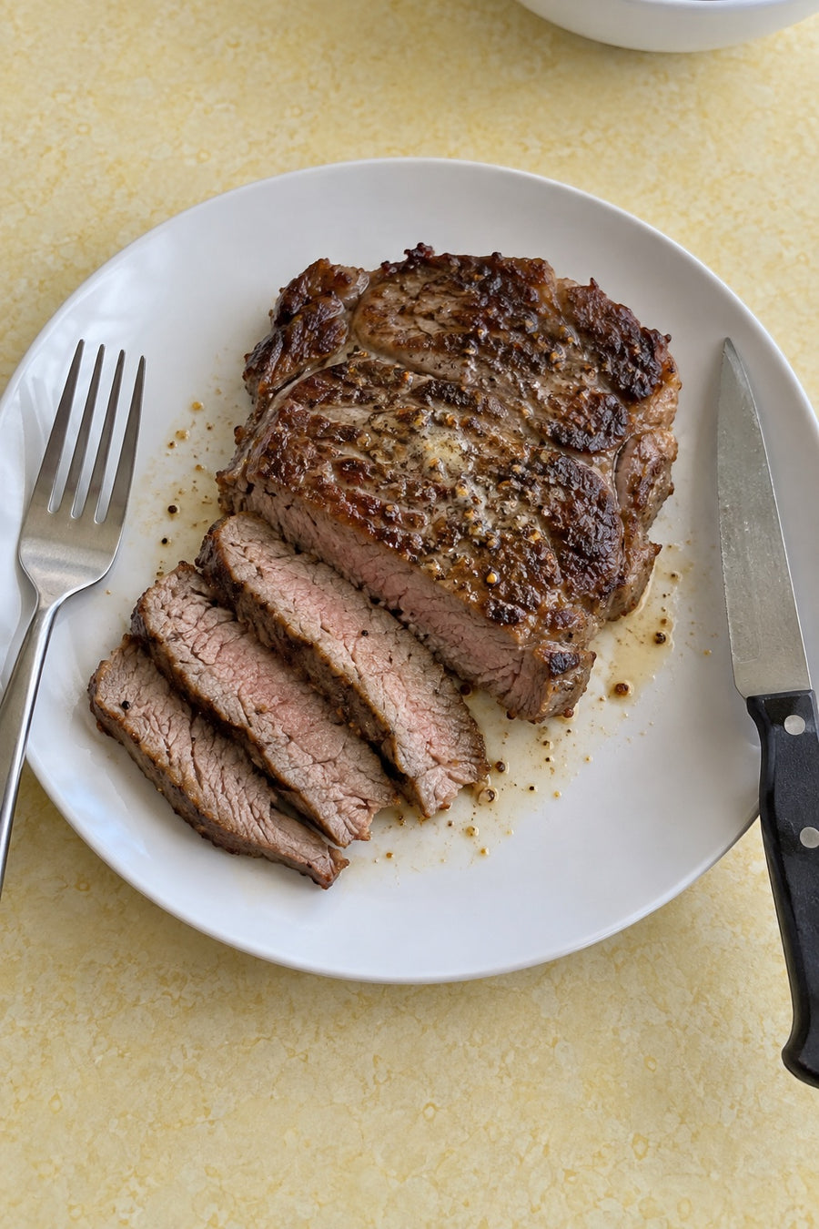 A pan-cooked chuck-eye steak partly sliced on a white plate with seasoned butter.