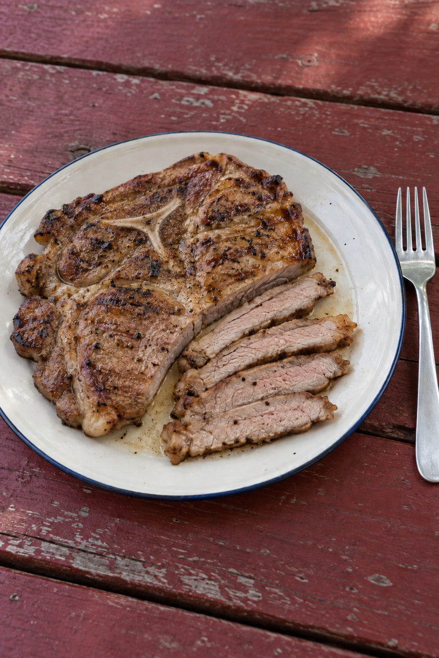 Grilled pork shoulder blade steak partly sliced around its bone on a simple outdoor plate.