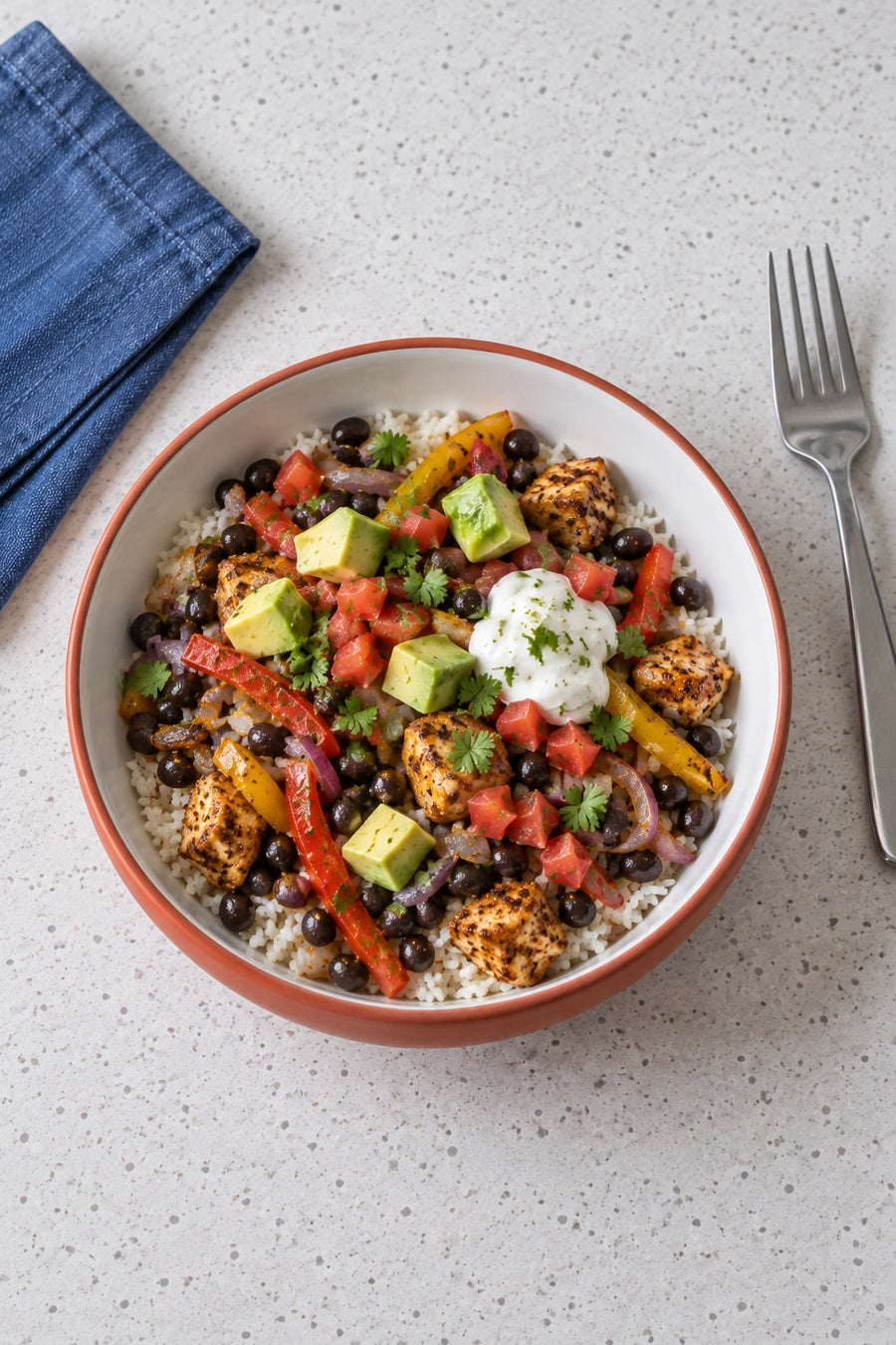 A chicken fajita rice bowl viewed from above with black beans, peppers, avocado, diced tomato and lime yogurt.