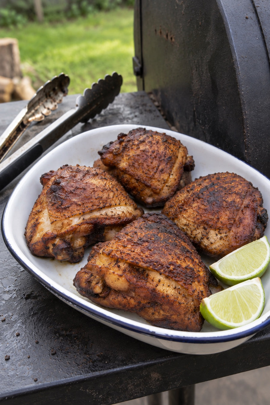 Smoked chicken thighs with lime beside a backyard smoker