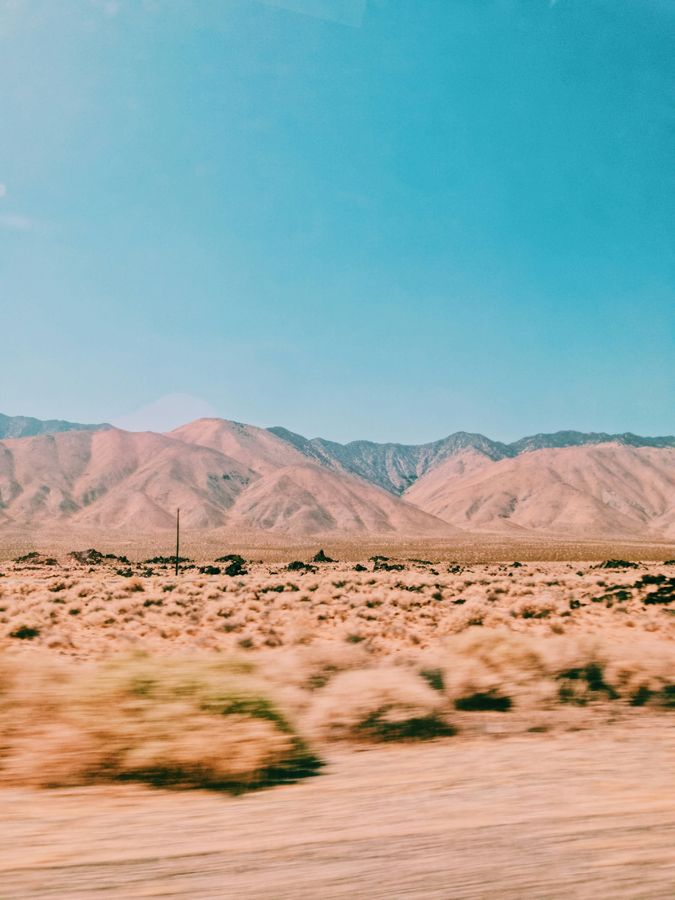Pale desert mountains and sandy scrubland beneath a bright blue sky.