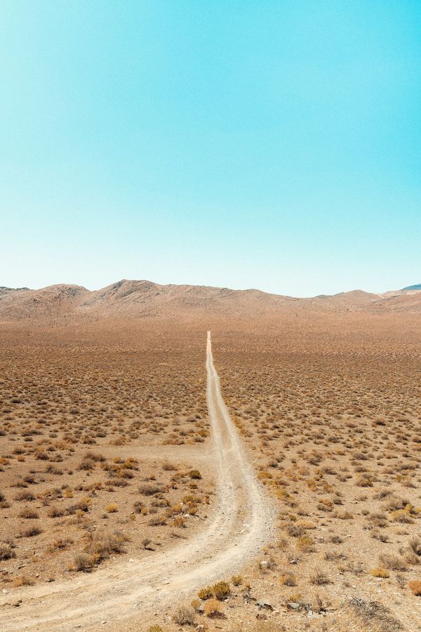 A dirt track winds through low desert scrub toward distant hills.